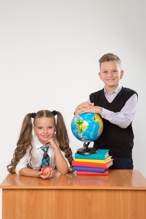 Happy boy and girl sit at a school desk, isolated on white background. Ideal for banners, registration forms, presentation, landings, presenting concept.の写真素材