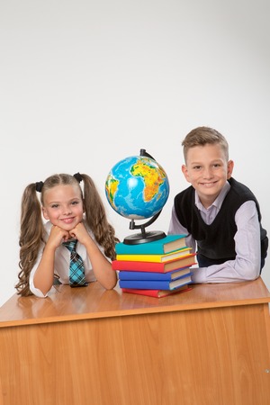 Happy boy and girl sit at a school desk, isolated on white background. Ideal for banners, registration forms, presentation, landings, presenting concept.の写真素材