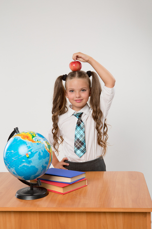 Happy little schoolgirl with red apple on her head, wearing white blouse , standing against white background. Back to school concept. Ideal for banners, registration forms, presentation.の写真素材