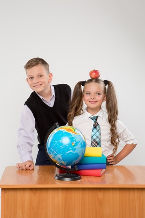 Happy boy and girl standing at a school desk, isolated on white background. Ideal for banners, registration forms, presentation, landings, presenting concept, school concept.の写真素材