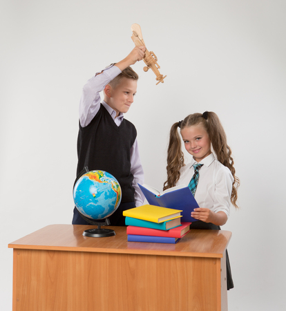 Happy boy and girl sit at a school desk, isolated on white background. Boy plays by airplane. Girl is reading a book. Ideal for banners, registration forms, presentation, landings, presenting concept.の写真素材