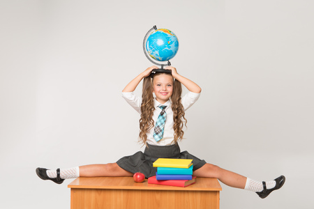 Happy little schoolgirl with globe on her head, wearing white blouse , standing against white background. Back to school concept. Ideal for banners, registration forms, presentation.の写真素材