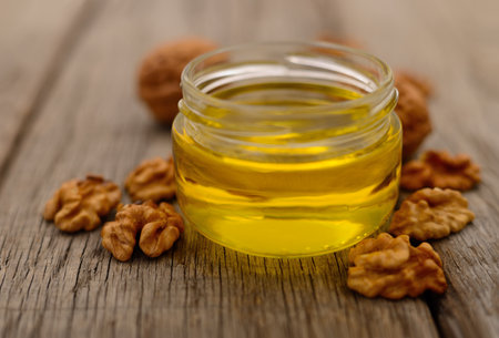 Walnut oil in glass jar, whole big peeled walnut kernel on wooden background.
