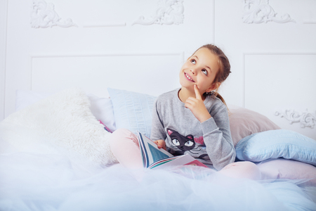 Girl child reading a book in bed. The concept of childhood and education.の写真素材