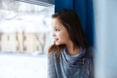 Little beautiful girl looking out the window. The concept of childhood and home.の写真素材