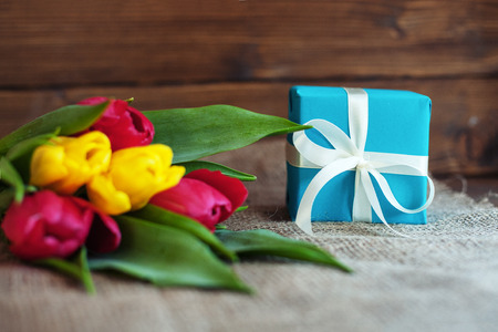 Beautiful tulips and blue gift on wooden background. Concept of holiday, birthday, Easter, March 8.の写真素材