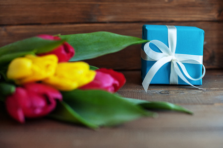 Colored tulips and blue gift on dark wooden background. Concept of holiday, birthday, Easter, March 8.の写真素材