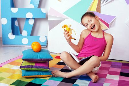 Cheerful child girl reading and eating a banana. The concept of education, training and childhood.の写真素材