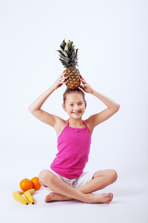 Funny child has oranges, pineapple and banana. The concept of healthy eating and vegetarianism.の写真素材