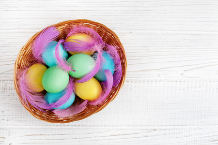 Colored eggs with feathers in basket. Top view. Concept Happy Easter.の写真素材