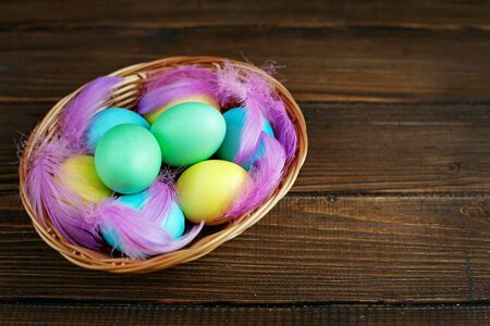 Colored eggs with feathers in a basket on a wooden background. Concept Happy Easter.
