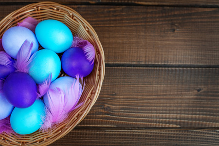 Colored eggs in a basket on a wooden background. Top view. Concept Happy Easter.の写真素材