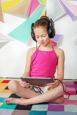 The girl child is sitting with a tablet. Listening audiobook. The concept of childhood and education.の写真素材