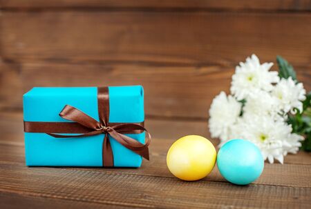 Light blue and yellow Easter eggs and a gift on a wooden background. Place for inscription. Concept Happy Easter.の写真素材