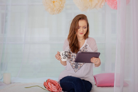 girl drinks coffee with the tablet. The concept of the Internet and lifestyle.の写真素材