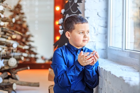 A little boy drinks tea and looks in the window. The child thinks. Concept Happy Christmas, New...