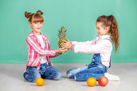 Two children with fruit, orange, pineapple and pomegranate. Sisters in jeans. The concept of a...