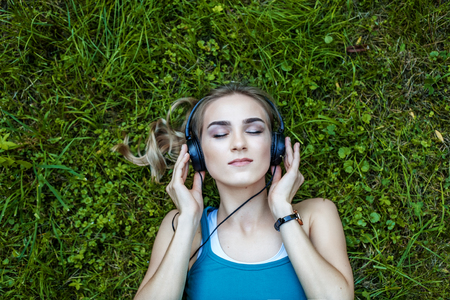 The young girl listens to the acdbook with the headphones. Park. Concept music, lifestyle and learning.の写真素材