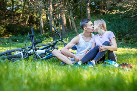Young happy couple in love kissing. Walking in the park on bicycles. The concept of cycling and a healthy lifestyle and love.の写真素材