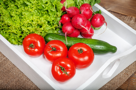 Tomatoes, cucumbers, radishes and lettuce on a white tray. Top view. The concept of healthy eating and vegetarianism.の写真素材