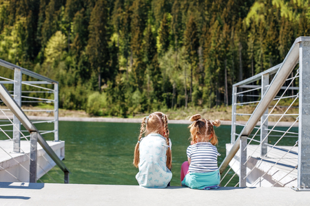 Little girls sit and look at the lake and the forest. Concept childhood, lifestyle, vacation, travel.の写真素材