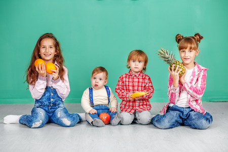 Four small children sit and hold fruit. Useful Fruits. The conceの写真素材