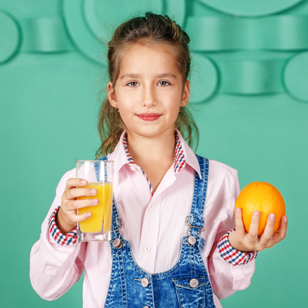 Kid girl drinks orange juice for breakfast. The concept of a heaの写真素材