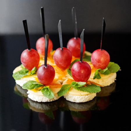 A lot of canapes with toast bread, cheese and grapes on a black background. Copy space. Concept for food, snacks, menu, restaurant, catering.の写真素材