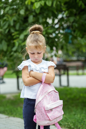 A small child stands offended on the street with a backpack. The concept of school, study, education, childhoodの写真素材
