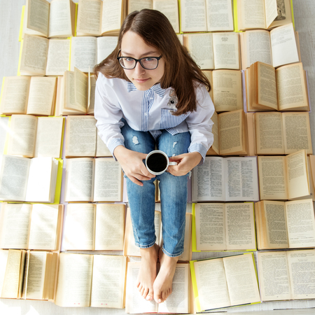 Young happy girl reading a book and drinking coffee. View from above. Concept for World Book Day,...