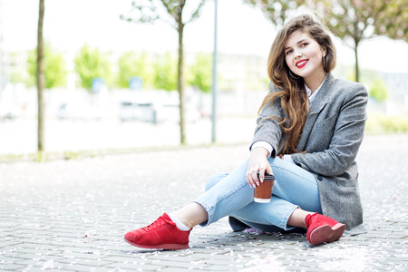 Happy female student sitting on the floor with coffee. Concept of lifestyle, urban, leisure, students.の写真素材