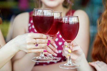 Glasses of red wine in female hands. Toast at a party. The concept of alcohol, holiday, meeting.の写真素材