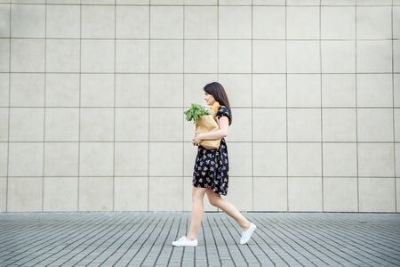 The girl comes with a bag with a baguette near the supermarket. The concept of shopping, lifestyle.
