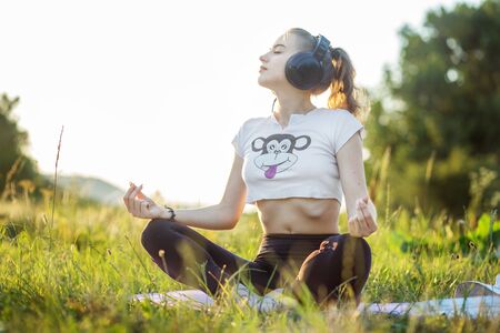 The girl listens to music on headphones. A woman is meditating. The combination of nature and man. Concept for lifestyle, music, relaxation.の写真素材