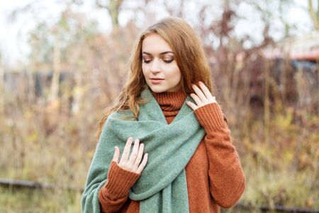 Adult beautiful woman in a light brown sweater and scarf. Nature. The concept of a lifestyle,...