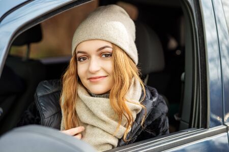 Young woman driving a car. Beige hat and scarf. Concept lifestyle, autumn, winter, auto driver.の写真素材