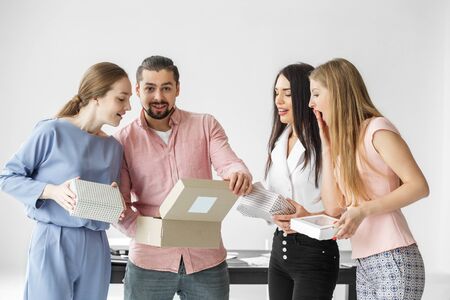 Colleagues at the office open boxes of Christmas presents. A group of employees. The concept of surprises, greetings and secret Santa.の写真素材