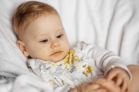 Feeding a baby vegetable puree. Dirty baby. The concept of childhood, care, first lure and baby food.の写真素材