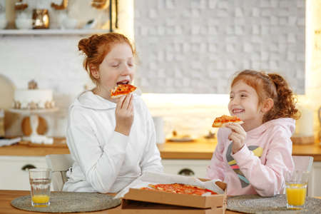 Young girls with red hair in the kitchen eating pizzaの写真素材