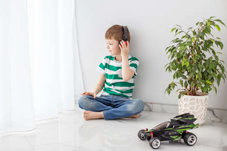 A boy in a green striped T-shirt sits on the floor enthusiastically reading a book, spends his...