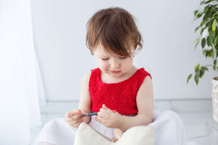 Little girl playing with makeup, holding a red pencil, little fashionista model.の写真素材