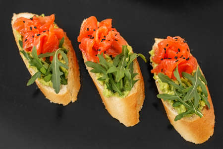Appetizer tartlets with red caviar and arugula on a black plate. Food snacks and appetizers for buffet.の写真素材