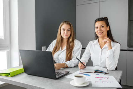 Two beautiful business women are working in the office. Business style clothing. White blouses.の写真素材