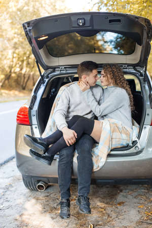 The guy and the girl are hugging in the trunk of the car. Autumn forest.の写真素材