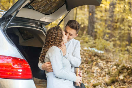 A loving couple walks in the autumn forest. Hot tea in a thermo mug. Happy laugh.