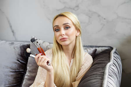 Young blonde woman holding a set of cosmetic brushes in her hand. Professional make-up artist.