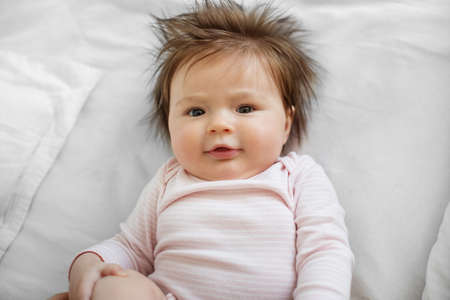 The baby is 3 months old. A beautiful newborn baby girl lies on a white sheet. Long black hairs.の写真素材