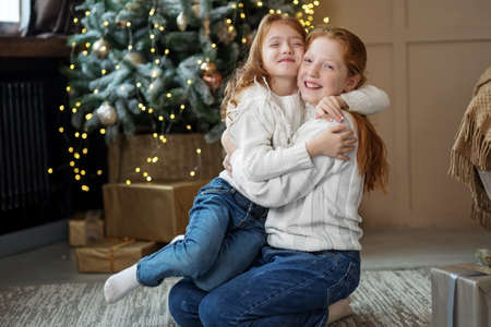 Two little sisters hug and laugh in the room. Winter holidays concept, merry christmas and family