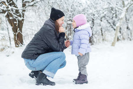Happy mom and little daughter spend time together and play. Walk in the snowy park.の写真素材