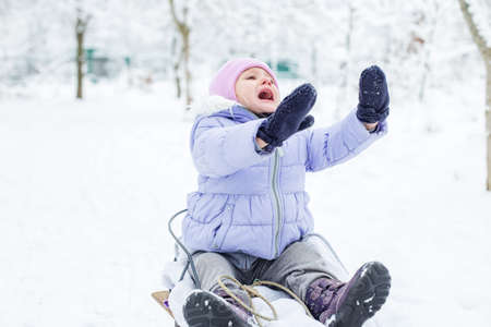 A frightened little kid is crying on a sled. Walk in the snowy park.の写真素材